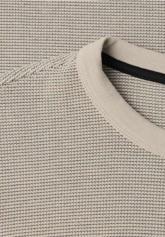 Nahaufnahme eines beigen Strickpullovers mit feinem Waffelmuster und Rundhalsausschnitt.