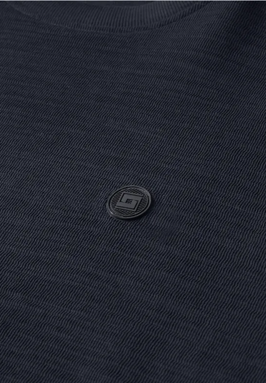 Gros plan d'un tissu noir texturé avec un petit logo rond discret au centre.