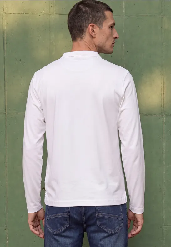 Ein Mann von hinten in weißem Langarmshirt und Jeans lehnt vor einer grünen Wand.