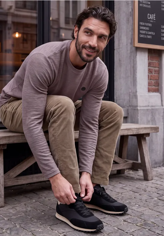 Ein Mann sitzt auf einer Bank vor einem Café und bindet seine Schuhe.