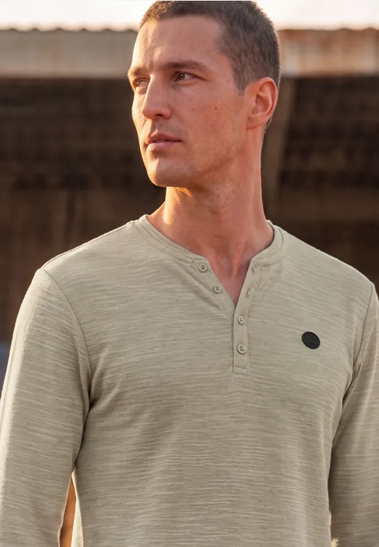 Mann in hellem Henley-Shirt blickt in die Ferne vor rustikalem Hintergrund