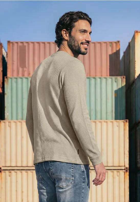 Ein Mann in legerer Kleidung steht vor bunten Containern und blickt über die Schulter.
