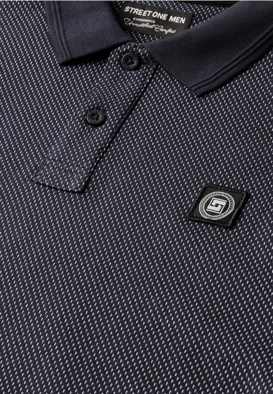 Nahaufnahme eines schwarzen Poloshirts mit feinem Muster, Kragen und einem markanten S1-Logo-Pin.