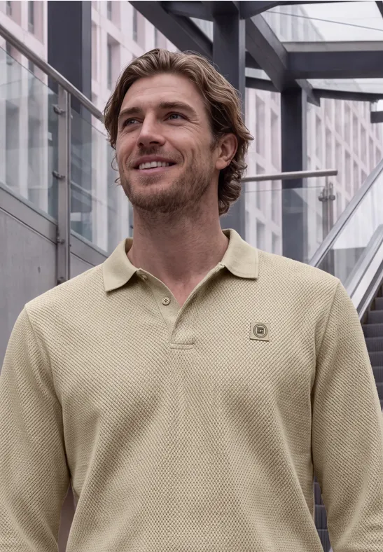 Ein lächelnder Mann im beigen Poloshirt steht vor einer modernen Glasfassade.