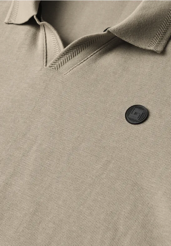 Gros plan sur un polo beige avec col et écusson rond noir, mettant en valeur la texture du tissu.