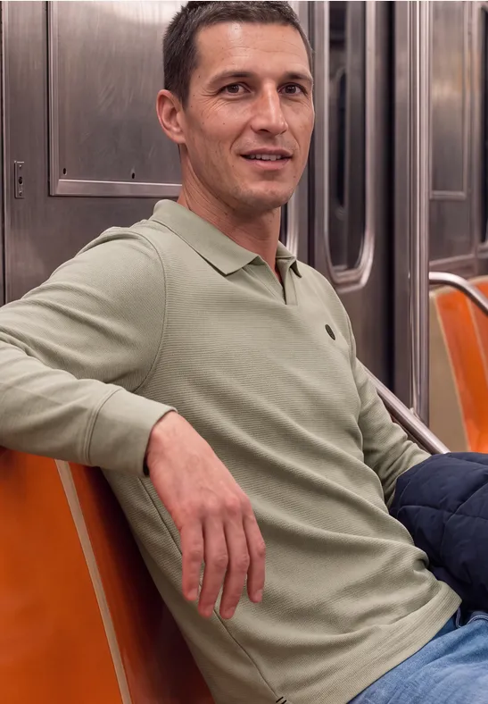 Un homme souriant est assis dans le métro sur des sièges orange.