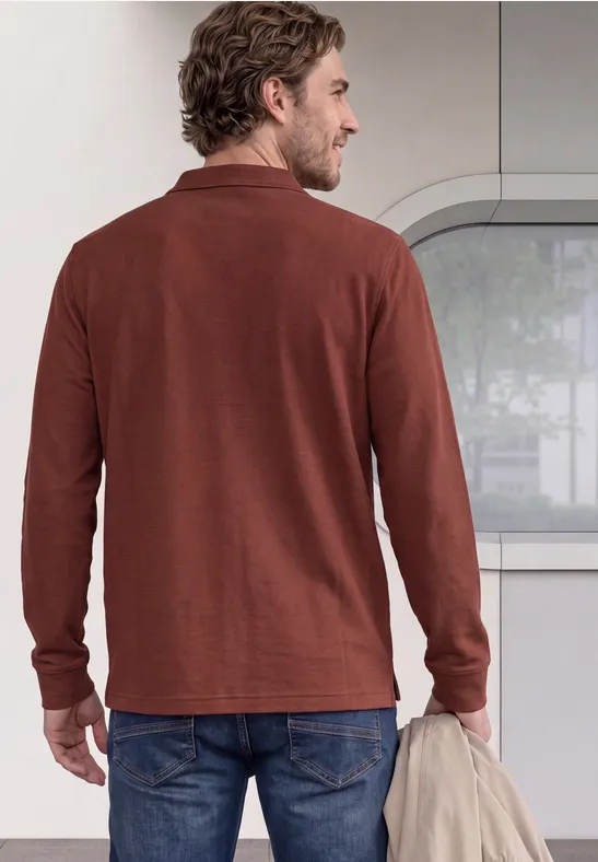 Ein Mann steht von hinten in einem braunen Langarmshirt und hält locker eine Jacke.