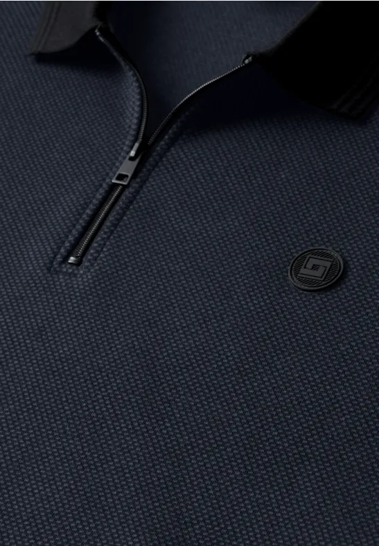 Gros plan sur un polo bleu marine texturé, demi-zip et logo rond brodé sur la poitrine.