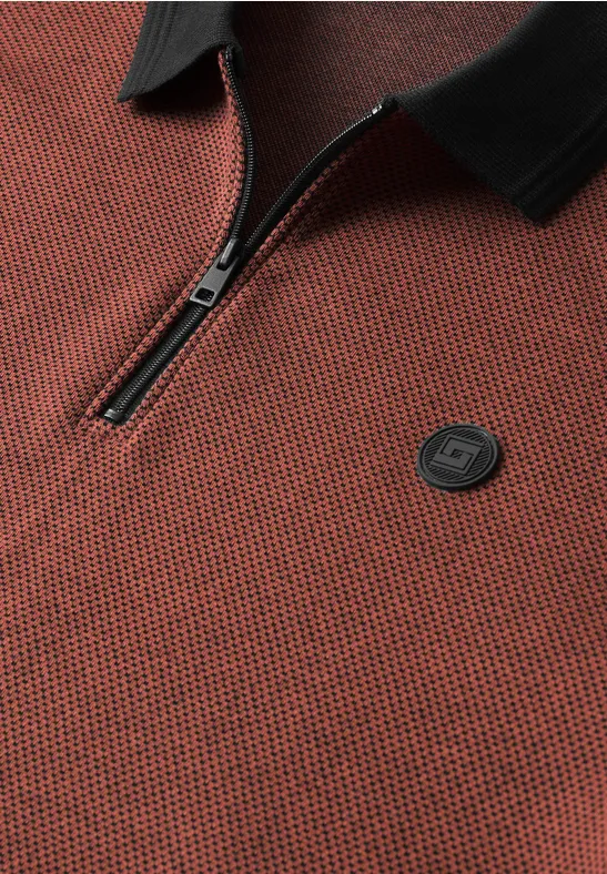 Nahaufnahme eines rot-schwarzen Poloshirts mit Reißverschluss und kleinem, runden Logo