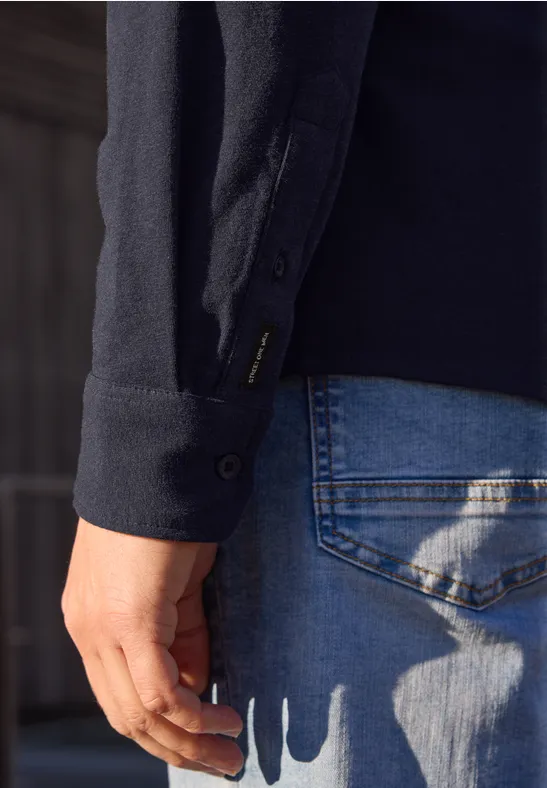 Person seitlich, trägt dunklen Pullover und blaue Jeans, Hand locker an der Seite.