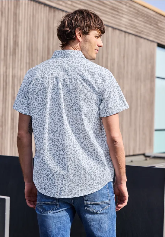 Ein Mann steht mit dem Rücken zur Kamera, trägt ein blau gemustertes Kurzarmhemd und Jeans.