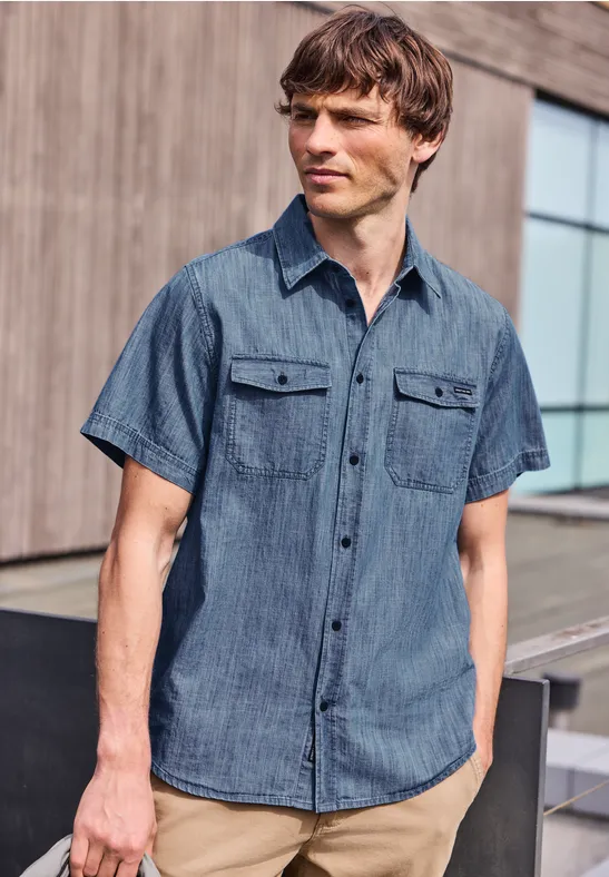 Mann in kurzärmligem Jeanshemd vor modernem Gebäude