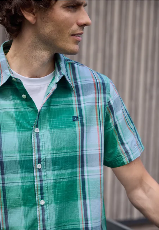 Eine Person trägt ein grünes kariertes Kurzarmhemd über einem weißen T-Shirt.