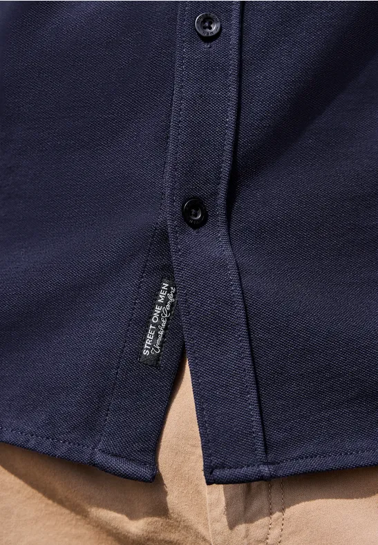 Dunkelblaues Hemd mit Knöpfen, seitlichem Schlitz und Labeldetail, auf beiger Hose.