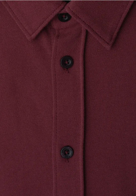 Close-up van een bordeauxrood overhemd met knopen en kraag.