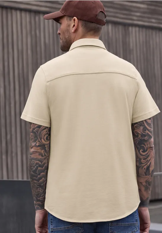 Een van achteren gefotografeerde man met rode pet, beige T-shirt en getatoeëerde armen.