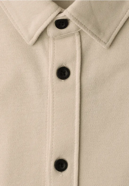 Close-up van een beige jasje met kraag en drie zwarte knopen.