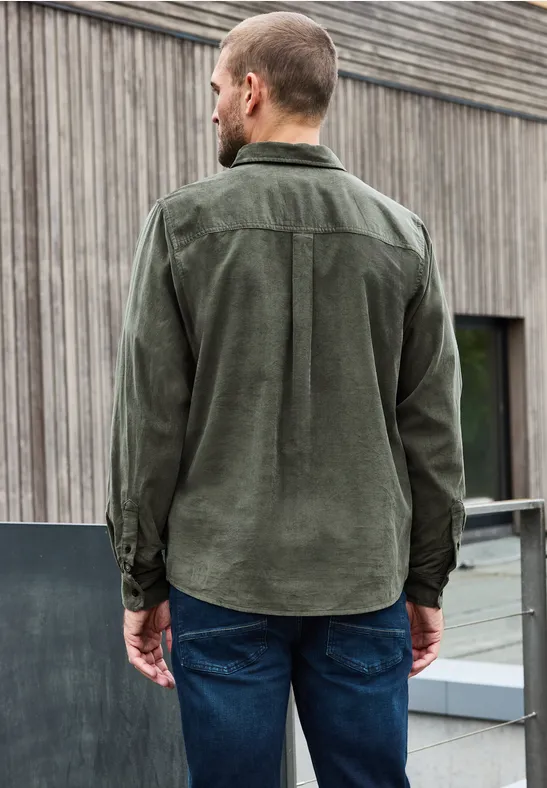 Mann von hinten in grüner Cordhemd und Jeans vor Holzfassade.