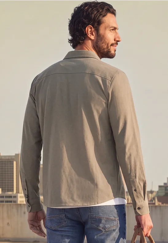 Ein Mann mit beigefarbenem Hemd steht auf einem Dach, im Hintergrund ist die Stadt zu sehen.