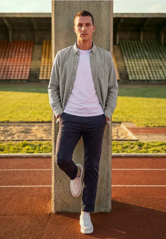 Mężczyzna opiera się o betonową kolumnę na bieżni przed trybunami stadionu.