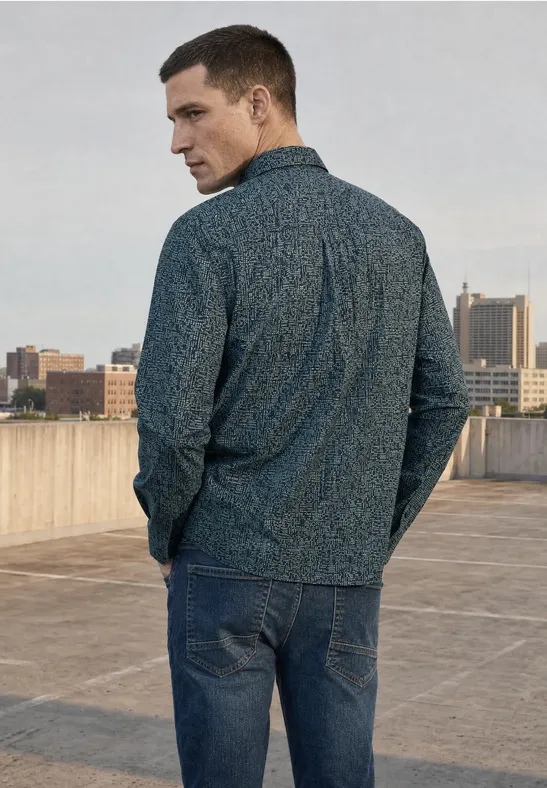 Ein Mann in Jeans und gemusterter Jacke steht auf einem Dach mit Stadtsilhouette im Hintergrund.