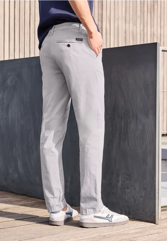 Man draagt lichtgrijze, casual broek en witte sneakers, staand buiten.