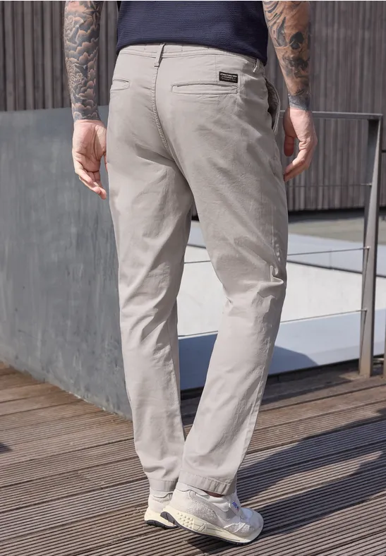 Ein Mann steht von hinten in hellen Chinohosen auf einer Holzterrasse neben einem Geländer.