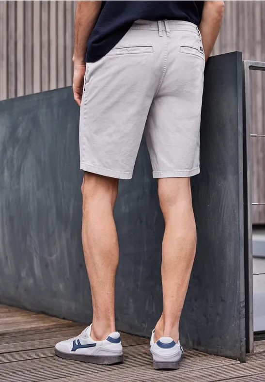 Mężczyzna opiera się o betonową ścianę, ma szare szorty i białe trampki.