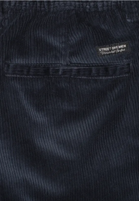 Close-up van donkerblauwe corduroybroek met zichtbare naad en klein logo-label.