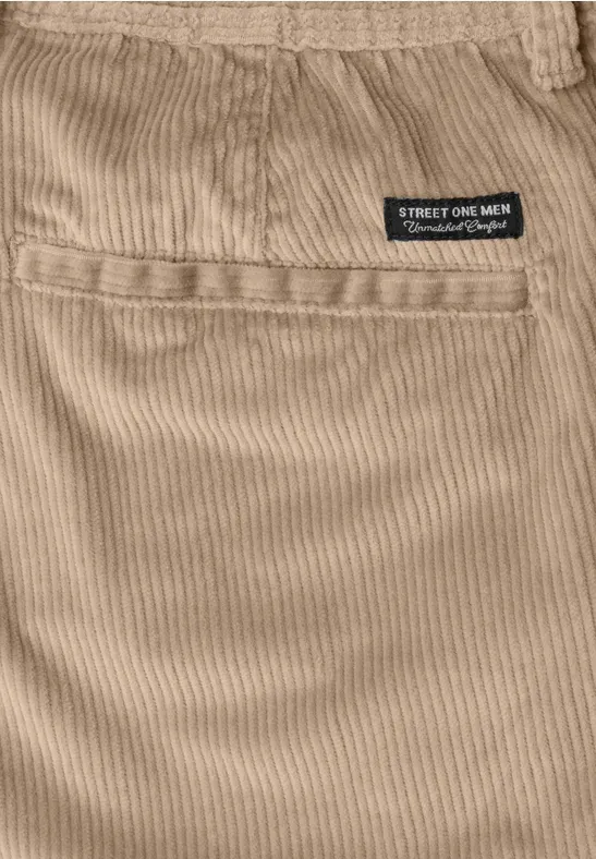 Nahaufnahme eines beigen Cordstoffs mit Tasche und kleinem schwarzen Etikett am Bund.