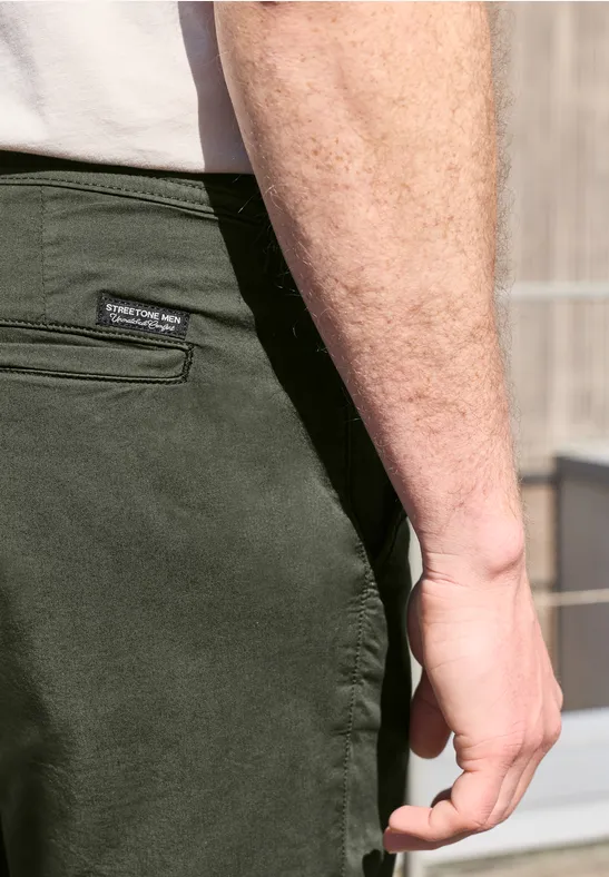 Nahaufnahme eines Mannes in olivgrüner Hose und weißem T-Shirt, Fokus auf Hand und Hüfte.