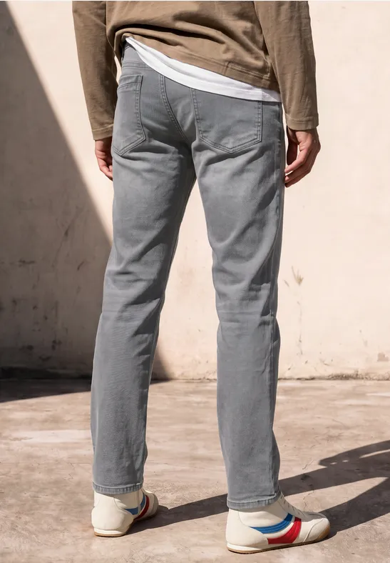 Vue de dos d'une personne portant un pantalon gris et des baskets blanches à rayures colorées devant un mur clair.