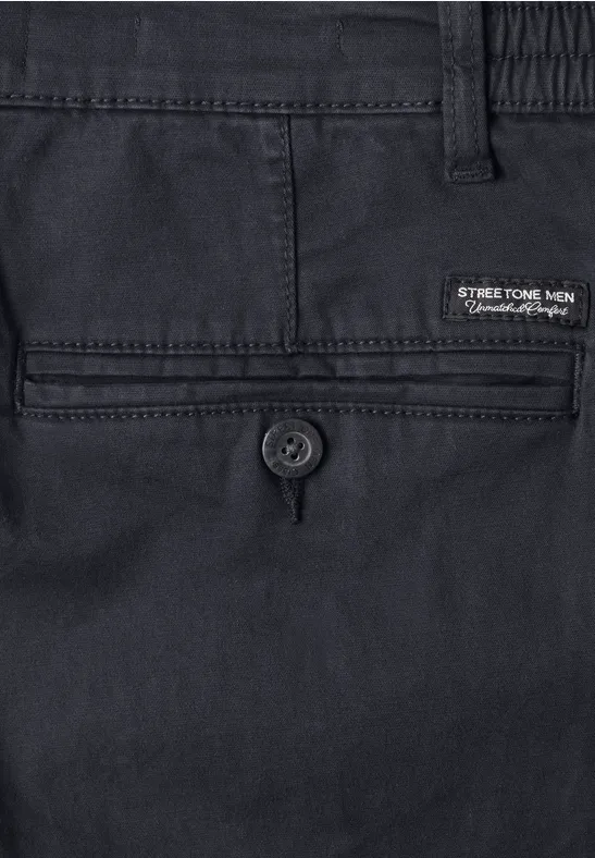 Close-up van een donkerblauwe herenbroek, achterzak met knoopsluiting en merklabel.