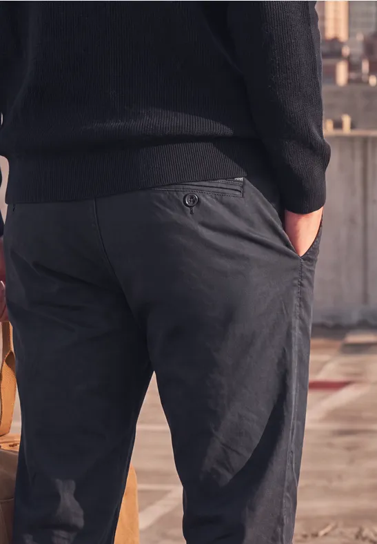 Close-up van een man van achteren in donkergrijze broek met handen in de zakken op een dak