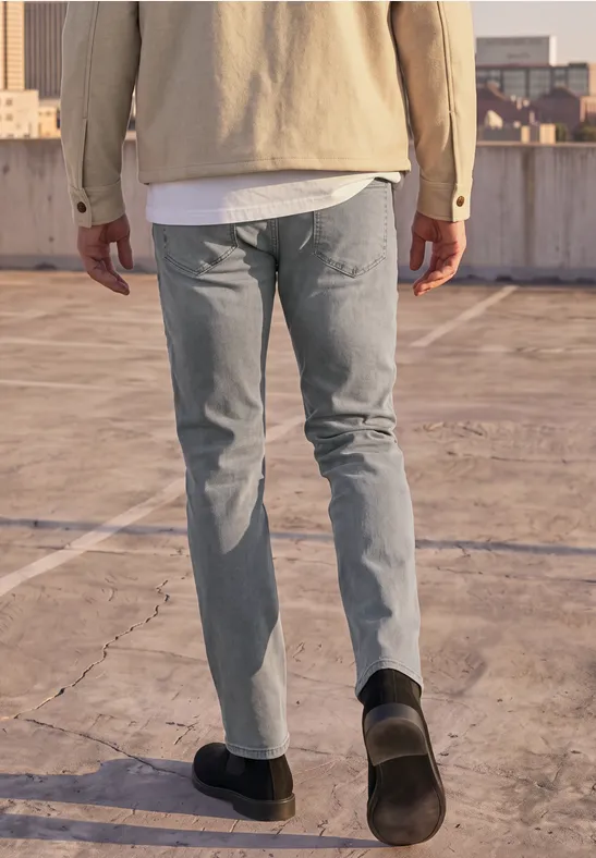 Ein Mann in Jeans, T-Shirt und Jacke geht auf einem leeren Dachparkdeck.