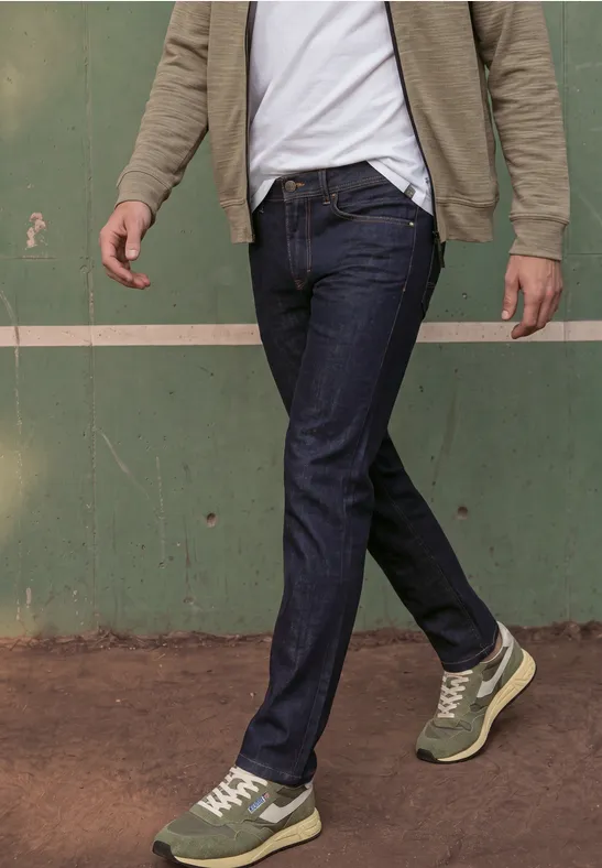 Ein Mann geht vorbei, trägt dunkle Jeans und grüne Sneaker vor einer grünen Wand.