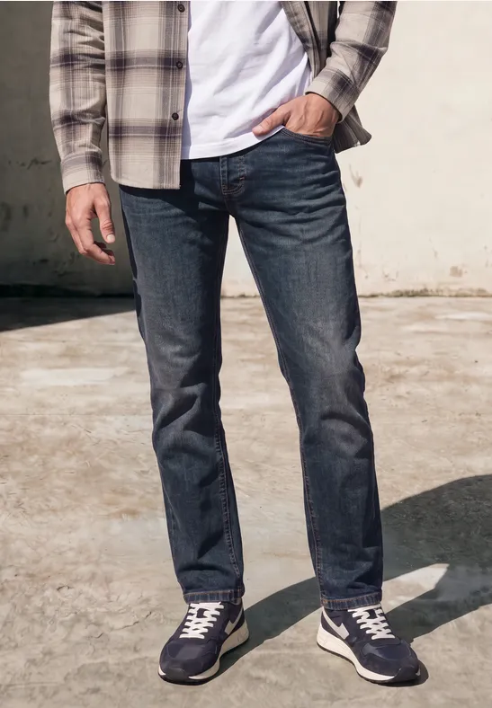 Mann im Freien, trägt dunkelblaue Jeans, weiße Sneakers, weißes T-Shirt und kariertes Hemd.