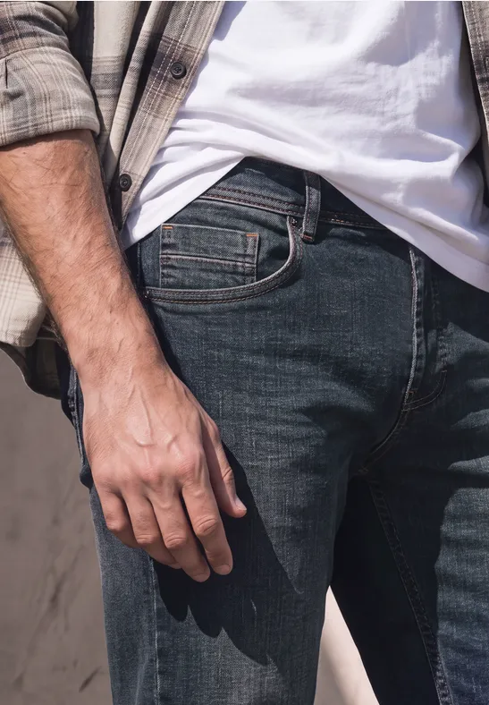 Nahaufnahme eines lässig gekleideten Mannes mit Hand an der Hüfte, dunkle Jeans und lockeres Hemd.