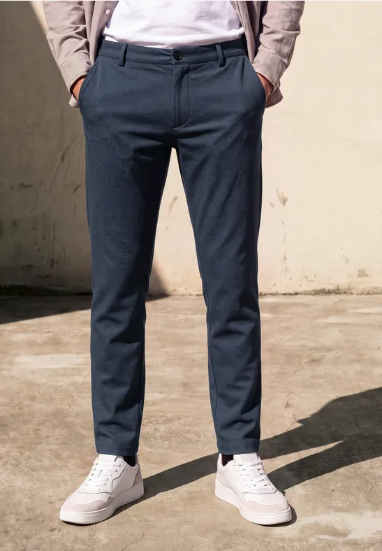 Eine Person trägt dunkelblaue Hose und weiße Sneaker vor einer hellen Wand.