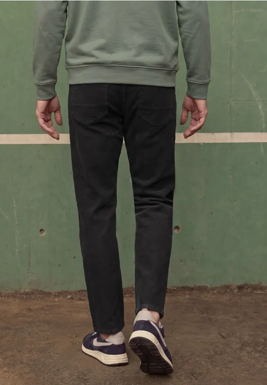Person von hinten, trägt schwarze Jeans und blaue Sneaker, steht vor einer grünen Wand.