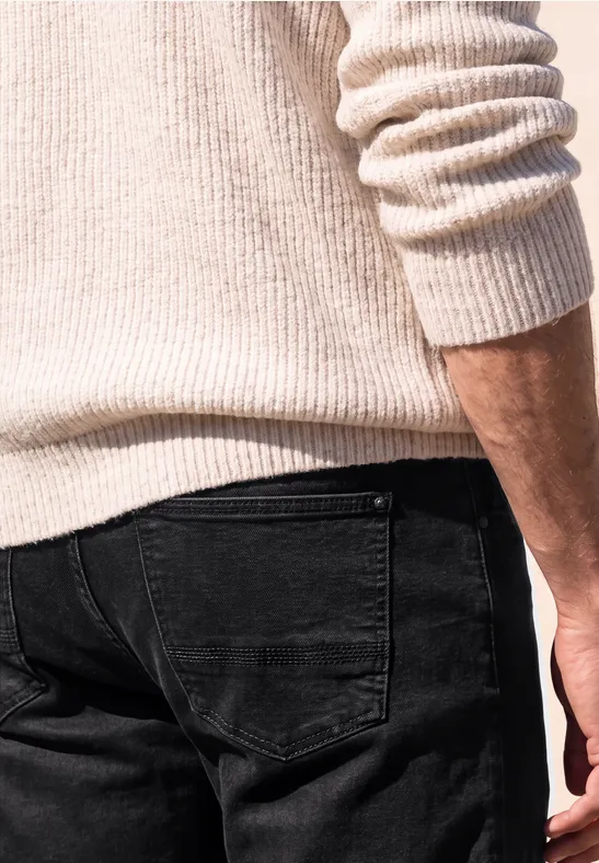 Rückenansicht einer Person in cremefarbenem Strickpullover und schwarzer Jeans.