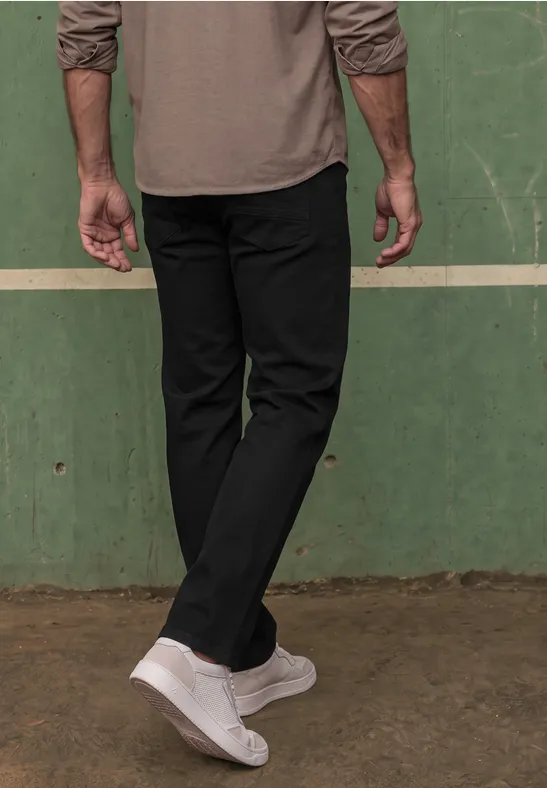 Untere Körperhälfte einer Person mit schwarzer Hose und weißen Sneakers vor grünem Wandhintergrund.