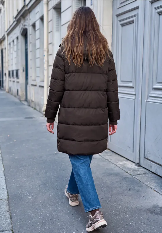 Frau in dunkler Steppjacke mit blauen Jeans und hellen Schuhen läuft weg.