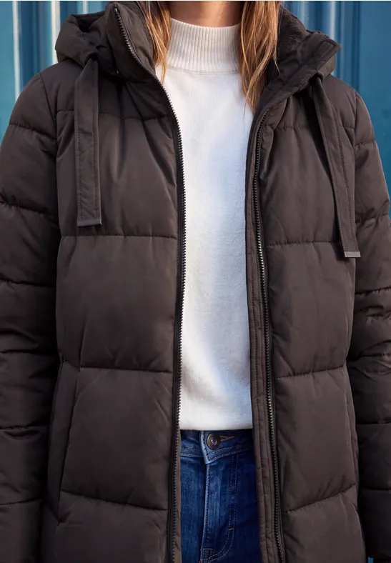Eine Person trägt eine schwarze Steppjacke, ein weißes T-Shirt und blaue Jeans.