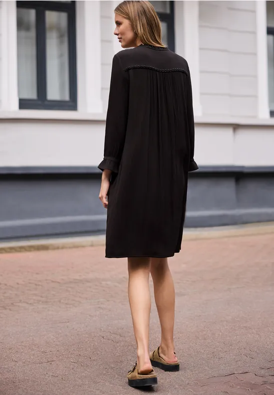 Frau von hinten in lockerem, schwarzem Kleid, die auf einer gepflasterten Straße geht.