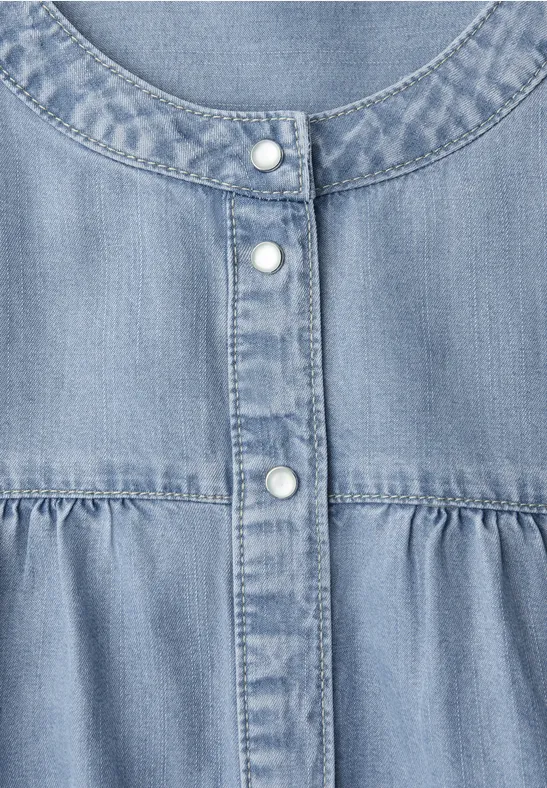 Hellblaue Denim-Bluse mit rundem Ausschnitt, Knopfleiste und Raffung unter der Brust.