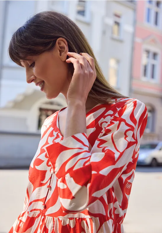 Een vrouw in een rood-witte bloemenjurk staat voor kleurrijke huizen in de stad.