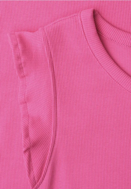 Close-up van een mouwloze roze ribgebreide top met ruches op de schouders.