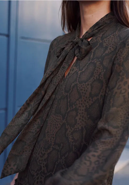 Eine dunkelgrüne Damenbluse mit Schlangenmuster und elegantem Schleifenkragen.