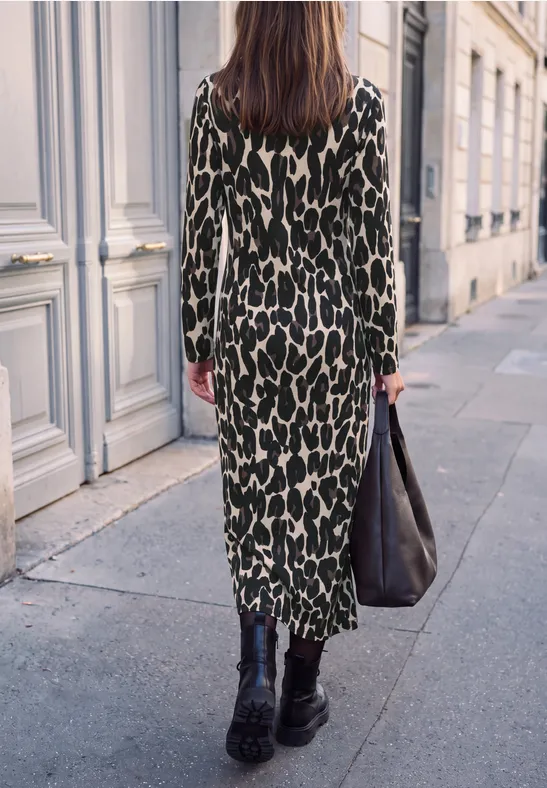 Frau geht auf Gehweg in lässigem Leoparden-Kleid, trägt schwarze Stiefel und große schwarze Tasche.